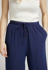 Pantalons en mélange d'élasthanne bleu marine avec une finition texturée, taille élastique, cordon de serrage ajustable et poches latérales.