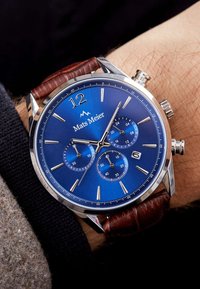 Chronograph-Uhr mit blauem Zifferblatt, silbernen Zeigern und der Ziffer 12, untergebracht in einem Gehäuse aus Edelstahl. Ausgestattet mit einem braunen Lederarmband und Unterzifferblättern.