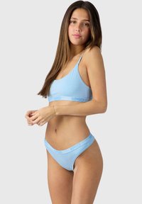 Light blue lingerie set featuring a bralette with thin straps and a matching thong, made from soft fabric with logo accents.