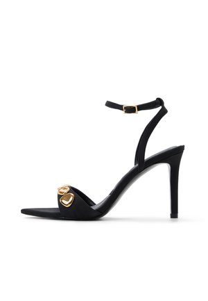 Sandalo nero con tacco alto, cinturino sottile alla caviglia, fibbia dorata e due dettagli decorativi dorati sulla fascia anteriore.