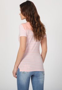 Camiseta de manga corta rosa claro con rayas blancas, con la parte trasera rosa sólido y aberturas laterales, combinada con jeans azules.
