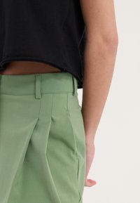 Groene plooirokbroeken van stof met een gladde textuur, voorzien van een platte tailleband en zijzakdetails, gecombineerd met een zwart cropped top.