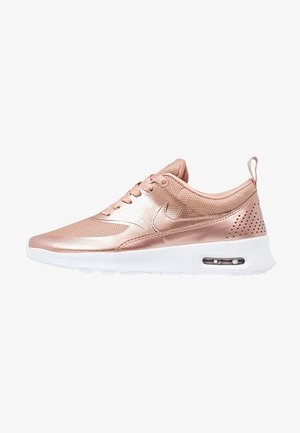 Chaussure de sport en or rose avec une finition métallique lisse, dessus en mesh, semelle intermédiaire blanche et détail de coussin d'air visible au talon.