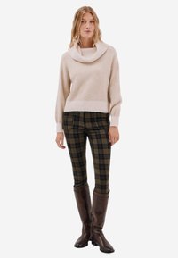Kremowy sweter z dekoltem w kapturek w zestawieniu z dopasowanymi spodniami w zieloną kratę i brązowymi kozakami za kolano. Miękka tekstura, luźny krój i akcenty w prążki.