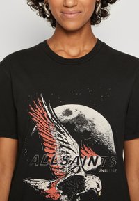 Svart bomulls t-shirt med en grafik av en örn med röda vingar mot en grå måne. Texten säger "ALLSAINTS UNIVERSE" under designen.