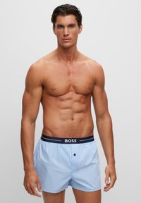 Boxers rayés bleu clair avec une ceinture élastique marine arborant le logo "BOSS", conçus en tissu doux pour le confort.