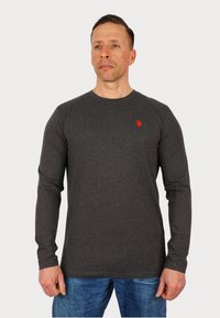 Tricou gri cu maneci lungi, fabricat dintr-un material moale, având un mic logo roșu pe pieptul stâng, asortat cu blugi albaștri.