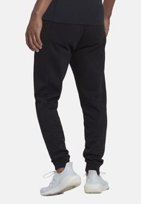 Svarta tapered joggers med elastisk midja och mudd, tillverkade av ett mjukt material. Bärs tillsammans med vita träningssneakers.