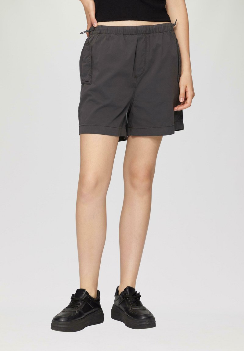Grijze shorts met een elastische tailleband, zijzakken en een relaxte pasvorm, gecombineerd met zwarte sneakers met een dikke zool.