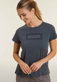 Camiseta de manga corta, gris oscuro, con cuello redondo. Presenta un panel brillante y texturizado con la palabra "FREDDY" en el centro. Tejido suave.