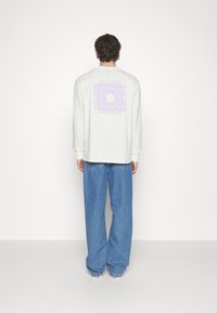 Light grey long-sleeve shirt with a purple graphic print on the back. Loose-fitting blue denim pants with a straight cut.