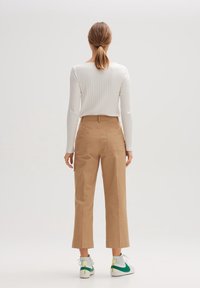 Haut à manches longues blanc côtelé associé à un pantalon taille haute beige et des baskets blanches avec des accents verts. Tenue épurée et décontractée.
