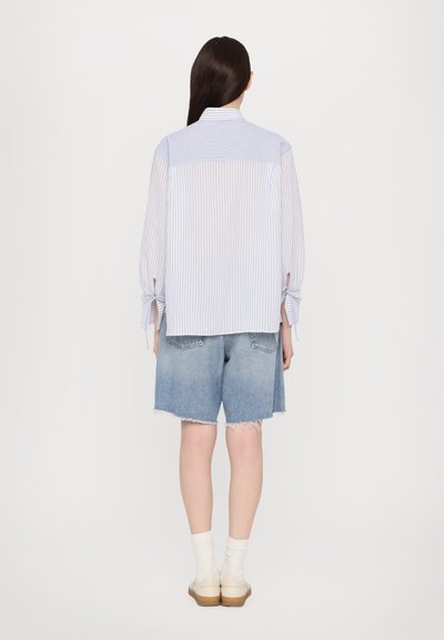 Lyseblå og hvite stripete skjorte med knyte detaljer på ermene, kombinert med shorts i denim med fransede kanter. Nøytral farget fottøy.