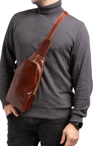 Borsa a tracolla in pelle marrone con finitura liscia, dotata di un compartimento principale con zip e una ampia tracolla regolabile.