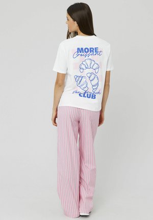 T-shirt blanc à manches courtes avec un texte bleu et des graphiques de croissant au dos, associé à un pantalon large rayé rose et blanc.