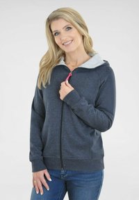 Grauer Reißverschluss-Hoodie mit einem hellgrauen Innenfutter, Kordelzug an der Kapuze, langen Ärmeln und Seitentaschen, kombiniert mit blauen Jeans.