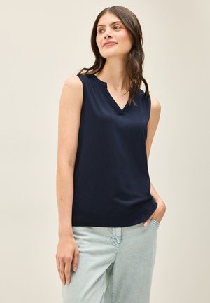 Haut sans manches bleu marine avec un décolleté en V, fabriqué en tissu lisse, avec un design simple et un léger stretch. Associé à un jean de couleur claire.