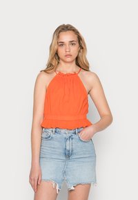 Top halter laranja com decote franzido e barra com babados, combinado com uma saia de ganga azul clara com barra irregular e bolsos frontais.