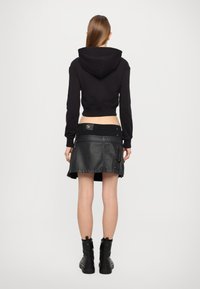 Svart kort ärmad huvtröja med huva och åtsittande ärmar, kombinerad med en svart läderkjol med blixtlås och midjedetalj. Svarta ankelskor.