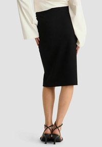 Zwarte pencil skirt met een getailleerd ontwerp, knie-lange snit en een gladde textuur. Gecombineerd met zwarte hakken met bandjes.