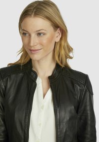 Black leather bomber jacket featuring ribbed shoulder accents, a rounded collar, and a zippered front. Worn over a white button-up shirt.