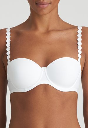Vrouw draagt een witte strapless beha met gegolfde bandjes en gevormde cups, getoond van schouders tot middenrif tegen een effen achtergrond.
