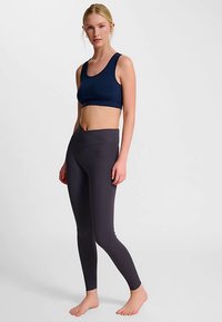 Marinblå atletisk crop top kombinerad med högmidjade, mörkgrå leggings. Slät tyg, figurnära design och sömlös midjedetalj.