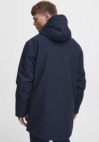 Navy blue hooded coat with a straight cut, featuring a textured fabric and visible stitching. Back view shows the length extending below the waist.
