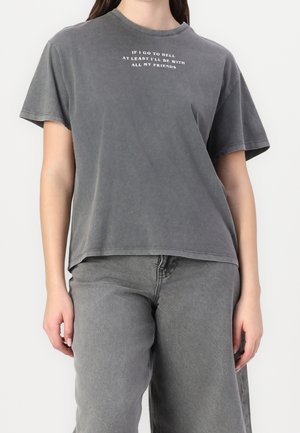 Personen bærer en falmet sort t-shirt med hvid tekst "Hvis jeg ender i helvede, vil jeg i det mindste være sammen med alle mine venner" og falmede sorte jeans.