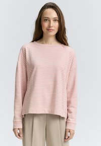 Top a maniche lunghe a righe rosa e bianche con scollo ampio e spacchi laterali, abbinato a pantaloni beige chiaro. Tessuto morbido.