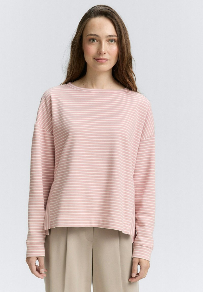 Top a maniche lunghe a righe rosa e bianche con scollo ampio e spacchi laterali, abbinato a pantaloni beige chiaro. Tessuto morbido.