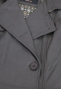 Graue Lederjacke mit einem breiten Kragen, zwei großen Knöpfen und einem gemusterten Innenfutter. Glatte Textur mit sauberen Nähten.