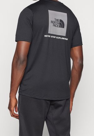 Person iført en sort t-shirt med The North Face-logo og teksten "Never Stop Exploring" på bagsiden.