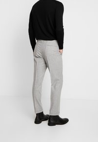 Lichtgrijze op maat gemaakte broeken met een gladde textuur, zijzakken en een omslagrand, gecombineerd met een zwarte lange mouw top en zwarte enkelboots.