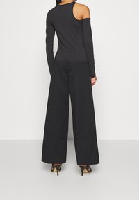 Maglia nera a maniche lunghe con design scoperto sulle spalle, abbinata a pantaloni neri a gamba larga e tacchi. Tessuto liscio e stile minimalista.