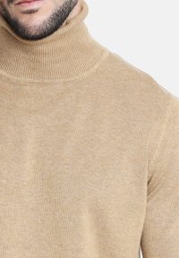 Suéter de cuello alto beige con cuello acanalado y tejido texturizado. La vista en primer plano resalta la suave tela y los detalles de costura bien hechos.