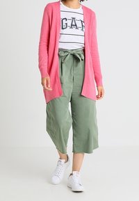 Růžový cardigan, bílý pruhovaný tričko s textem "GAP", olivově zelené široké kalhoty po kotníky a bílé tenisky. Měkký materiál a uvolněný střih.