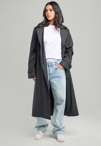 Long black raincoat with a glossy finish, double-breasted design, and large lapels, paired with a white t-shirt and light blue jeans.