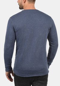 Donkerblauwe langetermijnhemd met een gestructureerde afwerking en spikkeldetail. Beschikt over een ronde halslijn en een lichtgerafeld zoom.