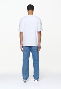 Camiseta blanca de algodón con mangas cortas, combinada con vaqueros de mezclilla azules. Los vaqueros tienen un corte recto y bolsillos traseros visibles.