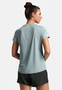 Svetle modré sportovní tričko s krátkým rukávem, strukturovaná tkanina a reflexní logo na zadní straně, spojeno s černými šortkami.