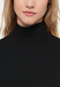 Maglione a collo alto nero a coste con un colletto aderente. Il tessuto ha una texture morbida e offre una vestibilità aderente attorno al collo.