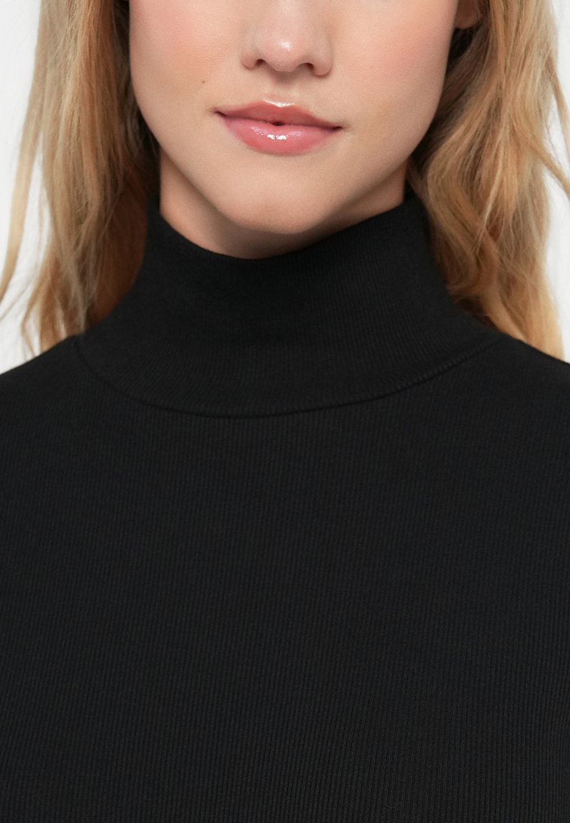 Maglione a collo alto nero a coste con un colletto aderente. Il tessuto ha una texture morbida e offre una vestibilità aderente attorno al collo.