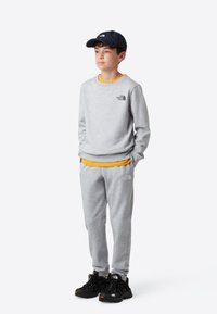 Lysegrå genser og matchende joggebukser med svart logo, lagvis over en gul skjorte. Svart caps og svarte treningssko fullfører antrekket.