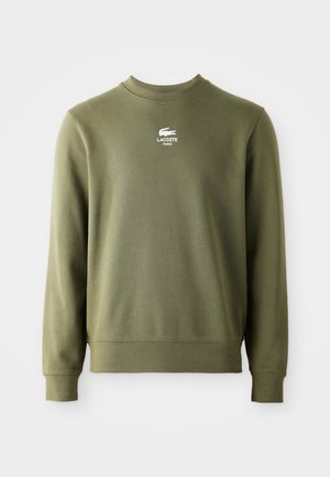 Sweatshirt vert olive avec un col rond, des poignets et un ourlet côtelés. Présente un logo Lacoste blanc sur la poitrine. Texture de tissu douce.