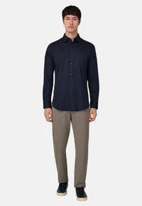 Chemise bleu marine à manches longues avec col et boutons, associée à un pantalon taupe clair et des baskets foncées. Texture lisse, coupe ajustée.