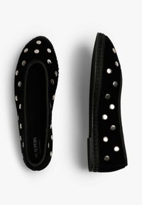 Zapatos slip-on de terciopelo negro con tachuelas plateadas redondas distribuidas de manera uniforme en la parte superior y los lados, suelas planas, un zapato mostrado desde arriba y el otro de lado.