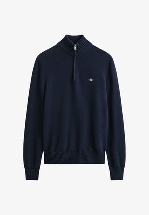 Marineblauwe gebreide trui met een hoge geribbelde kraag, een halve ritssluiting en een klein logodetail op de borst. Geribbelde manchetten en zoom.