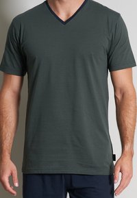 Tricou scurt, de culoare verde închis, dintr-un material moale și texturat, având un gât în V cu un accent bleumarin și dungi orizontale subtile.