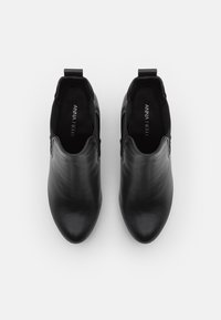 Mustat nahkaiset nilkkasaappaat, joissa on joustavat sivupaneelit ja vetonauhat, nähtynä ylhäältä valkoista taustaa vasten.